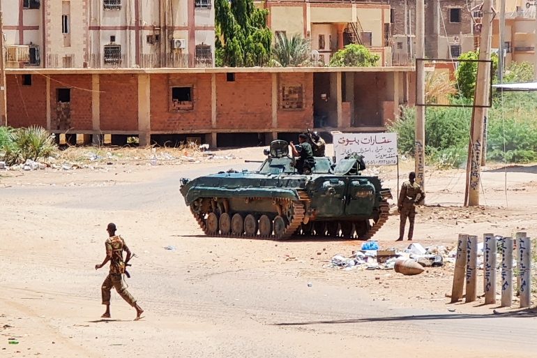 Sudanese Army sodliers walk near armoured vehicles stationed on a street in southern Khartoum, on May 6, 2023, amid ongoing fighting against the paramilitary Rapid Support Forces. Air strikes battered Sudan's capital on May 6, as fighting entered a fourth week only hours before the warring parties are to meet in Saudi Arabia for their first direct talks. (Photo by AFP)