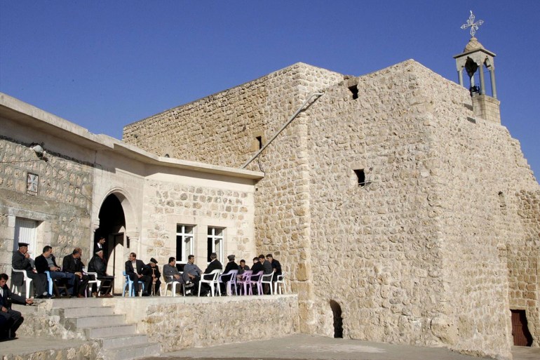 Assyrian men sit outside 7th century church of Mor Dodo, Haberli, Turkey, photo